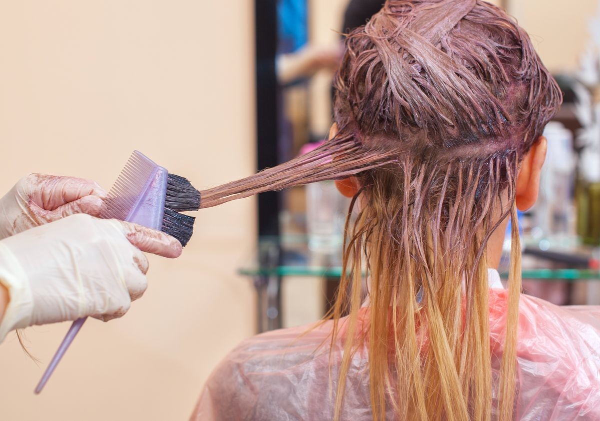 The hairdresser paints the woman's hair in white, apply the paint to her hair in the beauty salon.